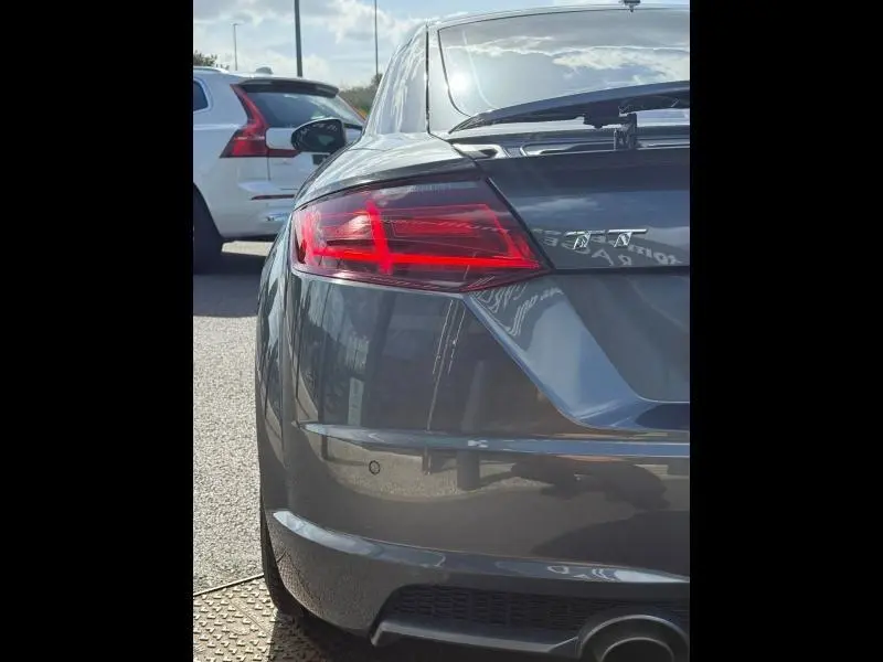 Vue 3/4 arrière droite d'une Audi TT Coupé 1.8 TFSI 2016 gris métallisé avec feux arrière LED et becquet arrière.