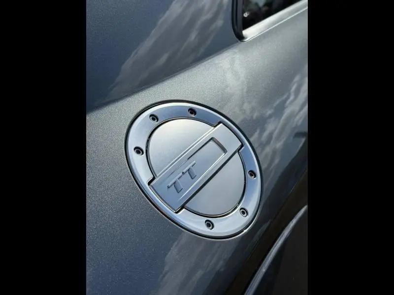 Gros plan sur la trappe à carburant argentée marquée TT, sur la carrosserie gris métallisé de l'Audi TT Coupé.