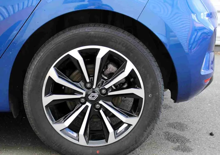 Gros plan sur la roue avant droite d'une Renault Clio bleu iron metal avec jante alliage noire et argentée.