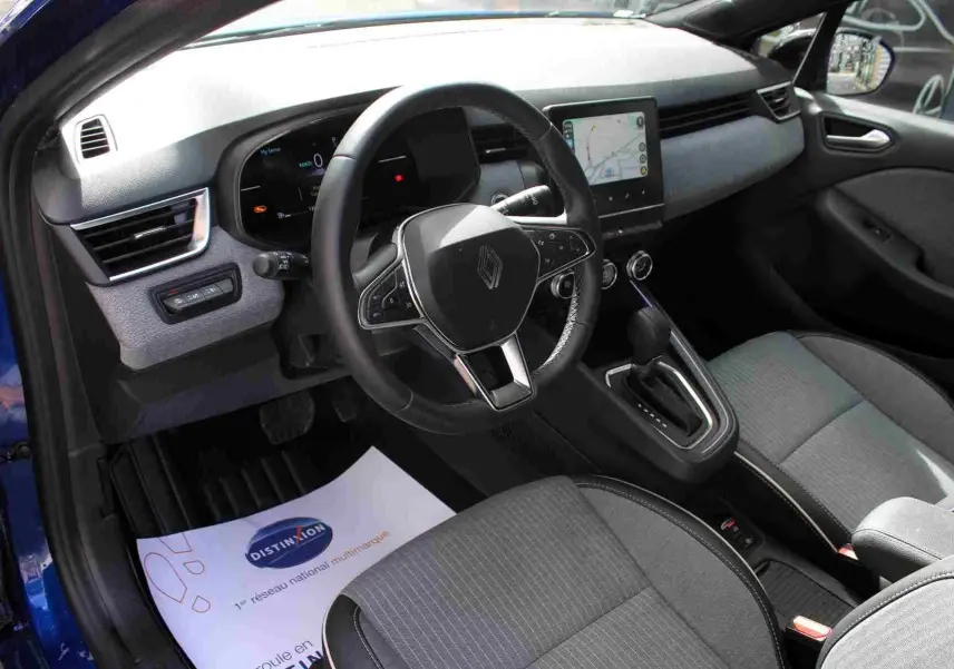 Vue intérieure côté conducteur de la Renault Clio bleu iron metal, volant multifonction et écran tactile central visible.
