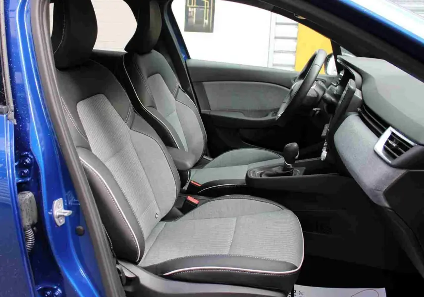 Vue intérieure côté gauche de la Renault Clio 2025 bleu iron metal, montrant les sièges avant gris et noir avec surpiqûres blanches.
