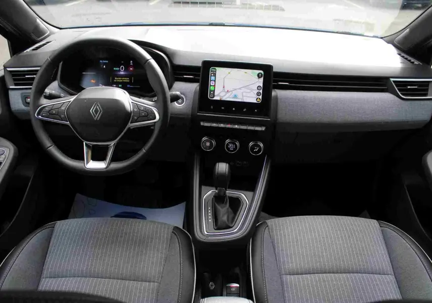 Vue intérieure avant de la Renault Clio hybride 2025, tableau de bord gris noir avec écran tactile central et volant multifonction.