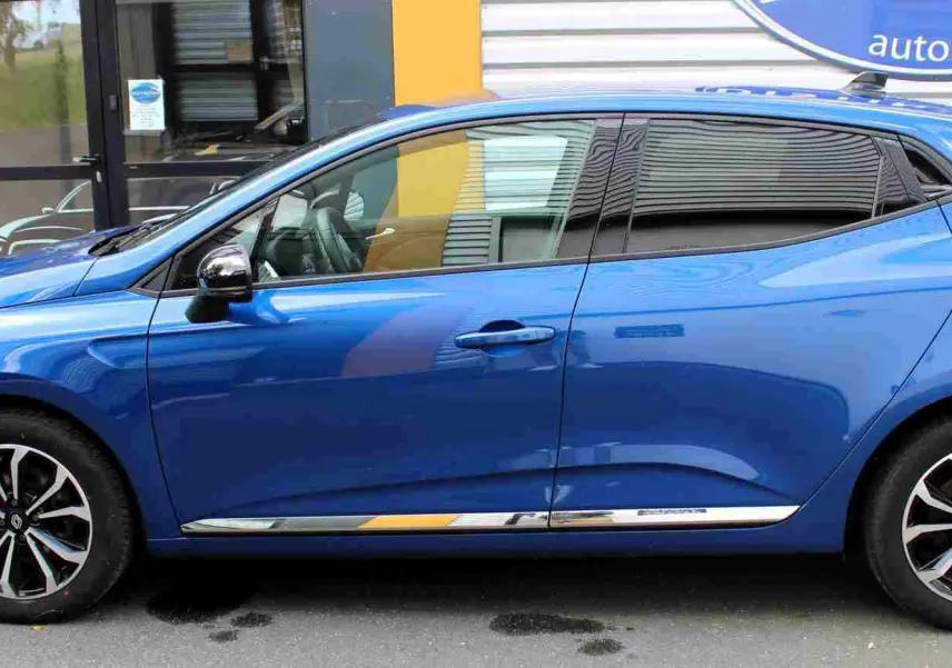Profil droit de la Renault Clio 2025 bleu Iron Metal avec jantes alliage et vitres teintées, garée devant un bâtiment.
