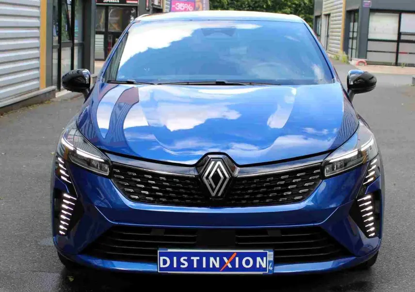 Vue frontale d'une Renault Clio 2025 bleu iron metal avec calandre noire et feux LED verticaux allumés.