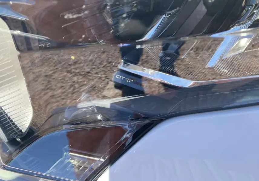 Gros plan sur le phare avant droit du Citroën Berlingo blanc 2025 avec détails chromés et marquage CITROËN visible.