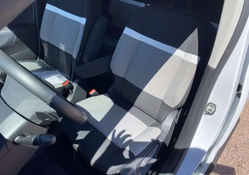 Vue intérieure côté conducteur du Citroën Berlingo blanc 2025, montrant les sièges avant en tissu gris bicolore.