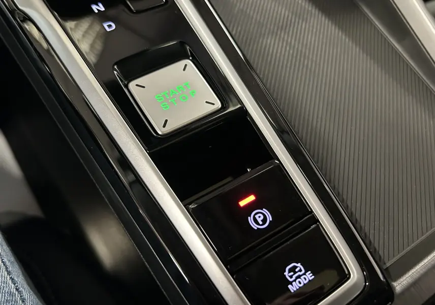 Gros plan sur la console centrale du MG ZS Hybrid+ 197 Luxury, avec bouton Start/Stop vert et commandes de mode et frein à main.