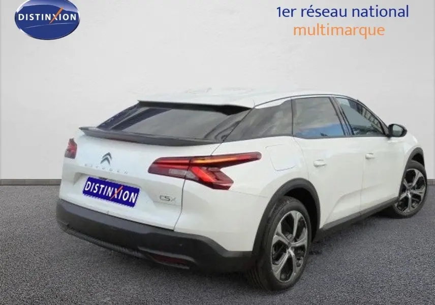 Vue 3/4 arrière droite d'une Citroën C5 X blanche métallisée avec feux LED et jantes bi-ton sur fond neutre.