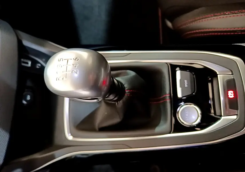 Gros plan sur levier de vitesses manuel argenté et console centrale noire avec surpiqûres rouges dans Peugeot 308 gris foncé.