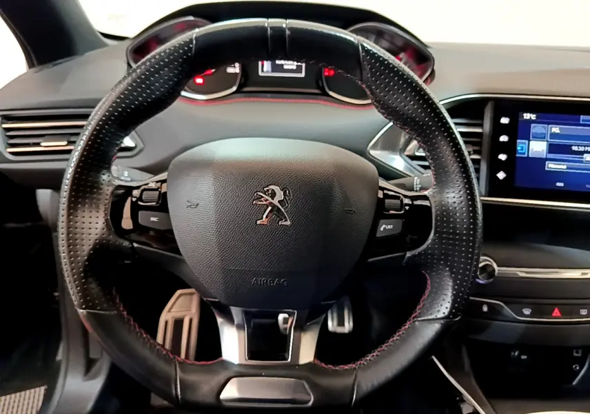 Vue centrée sur le volant cuir perforé avec surpiqûres rouges de la Peugeot 308 GT Line 2016, tableau de bord et écran tactile visibles.