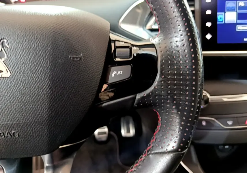 Gros plan sur le volant cuir perforé avec surpiqûres rouges de la Peugeot 308 GT Line 2016, tableau de bord tactile visible.