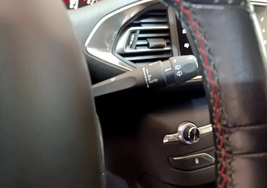 Gros plan sur la commande d’essuie-glace et la sortie d’air côté gauche du tableau de bord noir du Peugeot 308 gris foncé.