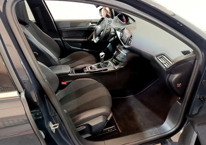 Intérieur côté conducteur d'une Peugeot 308 gris foncé, volant cuir, console centrale avec boîte manuelle et écran tactile.