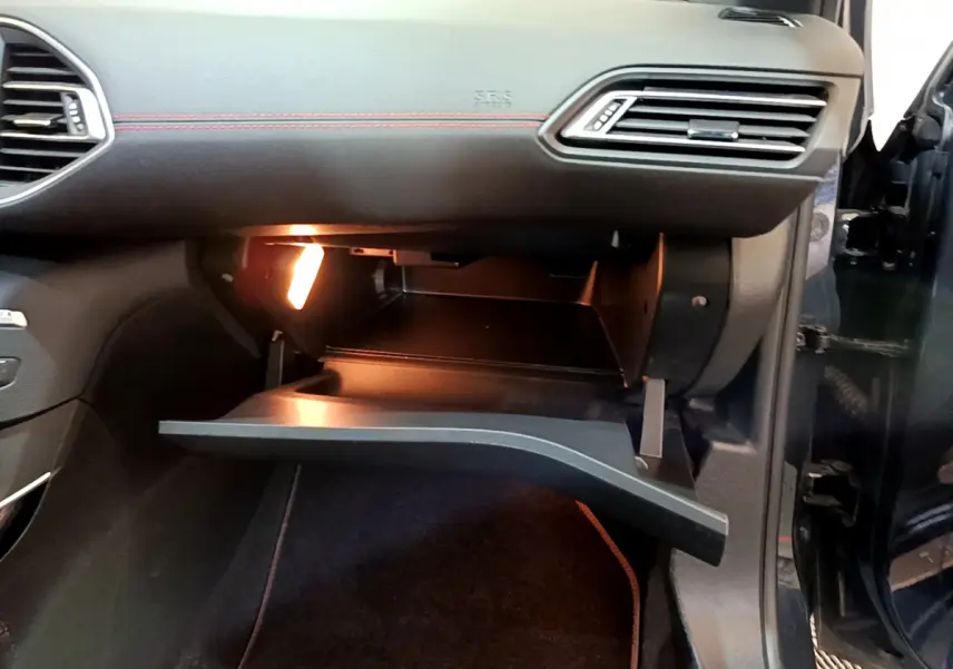 Gros plan sur la boîte à gants ouverte éclairée côté passager d'une Peugeot 308 gris foncé 2016.