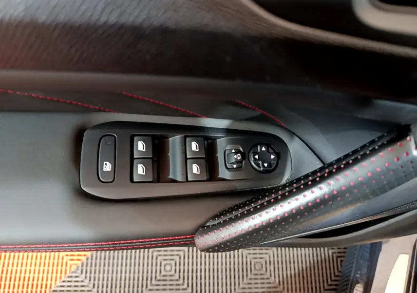 Commandes des vitres électriques et réglages des rétroviseurs sur la porte côté conducteur d'une Peugeot 308 gris foncé, avec surpiqûres rouges.