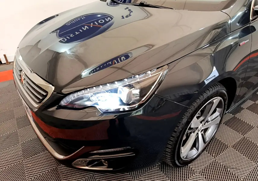 Vue 3/4 avant droit d'une Peugeot 308 gris foncé avec phares LED allumés et jantes alliage visibles.