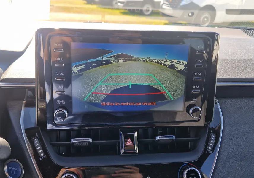 Vue intérieure centrée sur l'écran multimédia affichant la caméra de recul d'une Toyota Corolla hybride gris clair de 2019.