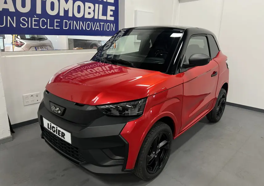 Vue 3/4 avant droite d'une LIGIER JS50 BEV 8KWH ELITE rouge avec toit noir et jantes alu noires en intérieur showroom.