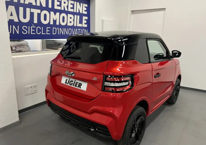 Vue 3/4 arrière droite de la LIGIER JS50 BEV 8KWH ELITE rouge avec toit noir et jantes alu noires en intérieur showroom.