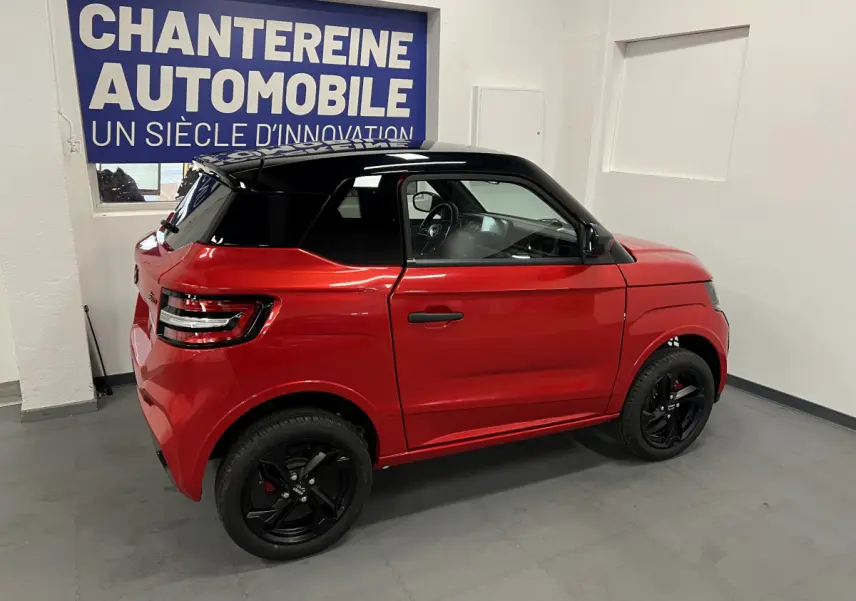 Vue de profil droit d'une LIGIER JS50 BEV 8KWH ELITE rouge avec toit noir et jantes alu noires en intérieur showroom.