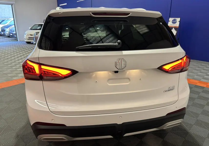 Vue arrière d’un MG ZS Hybrid+ 197 Luxury blanc Dover avec feux allumés et logo MG visible sur le hayon.
