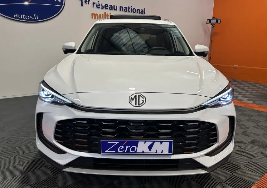 Vue frontale du MG ZS Hybrid+ 197 Luxury en blanc Dover, avec phares LED allumés et calandre noire imposante.