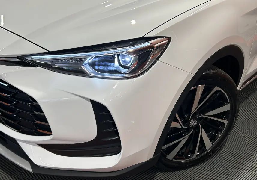 Gros plan sur l'avant droit blanc Dover White du MG ZS Hybrid+ 197 Luxury, mettant en valeur le phare LED et la jante noire brillante.