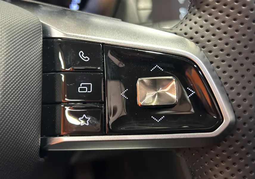 Gros plan sur les commandes multifonctions en noir brillant du volant perforé du MG MOTOR ZS Hybrid+ 197 LUXURY blanc.