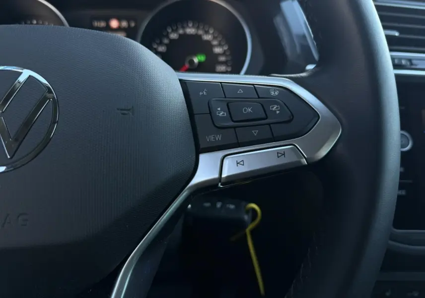 Gros plan sur le volant multifonctions cuir du Volkswagen Tiguan 2024, boutons de commande et logo VW visibles.