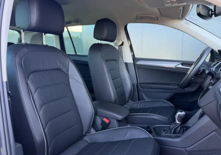 Vue intérieure côté gauche du Volkswagen Tiguan 2024, sièges cuir Vienna noirs avec surpiqûres grises et console centrale.