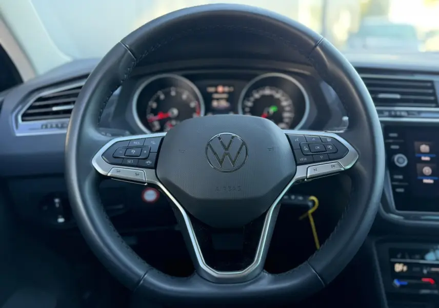 Gros plan sur le volant cuir multifonctions noir du Volkswagen Tiguan 2024 avec tableau de bord et écran tactile en arrière-plan.