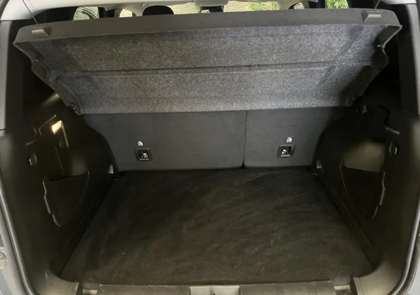 Coffre ouvert du Jeep Renegade gris 2024 montrant le plancher modulable et les rangements latéraux noirs.