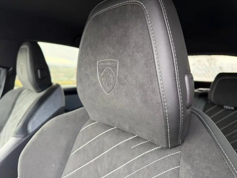 Gros plan sur l'appui-tête avant en Alcantara gris avec logo Peugeot embossé, intérieur du 3008 GT bleu 2024.