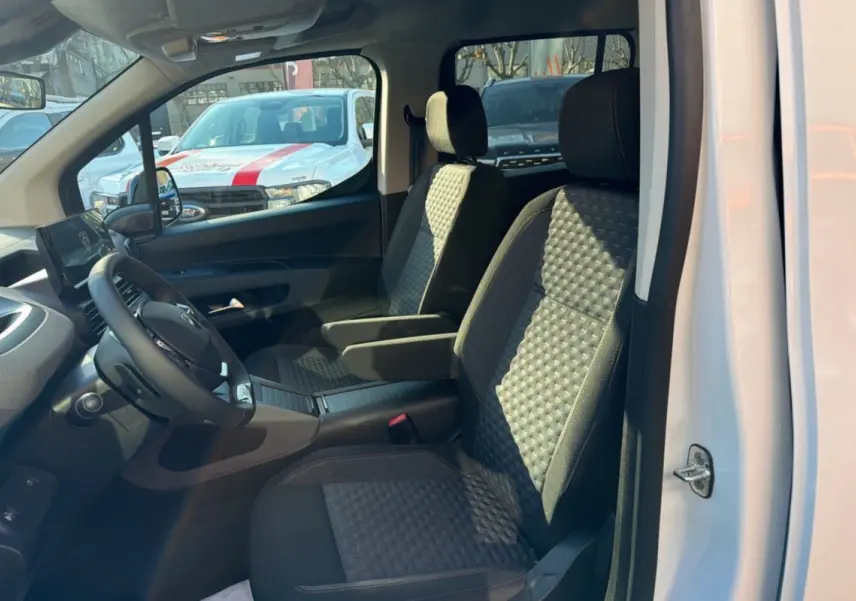 Vue intérieure côté conducteur du Peugeot Rifter blanc kaolin 2025, sièges tissu avec accoudoirs et volant cuir multifonctions.