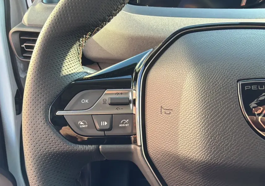 Gros plan sur le volant cuir perforé côté gauche du Peugeot Rifter Blanc Kaolin, avec commandes multifonctions intégrées.