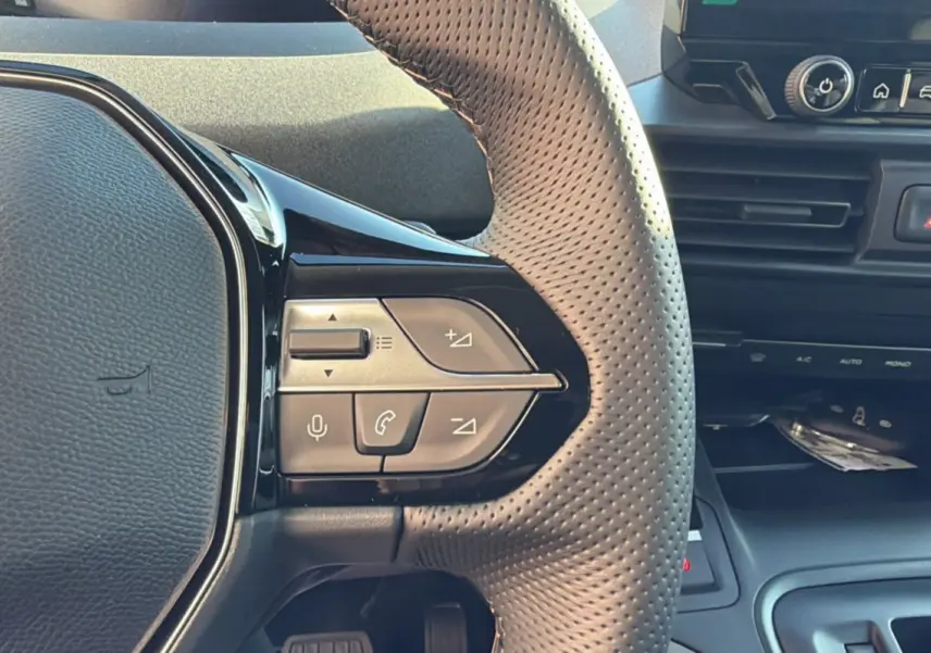 Gros plan sur le volant cuir perforé du Peugeot Rifter 2025, avec commandes multifonctions et tableau de bord noir.