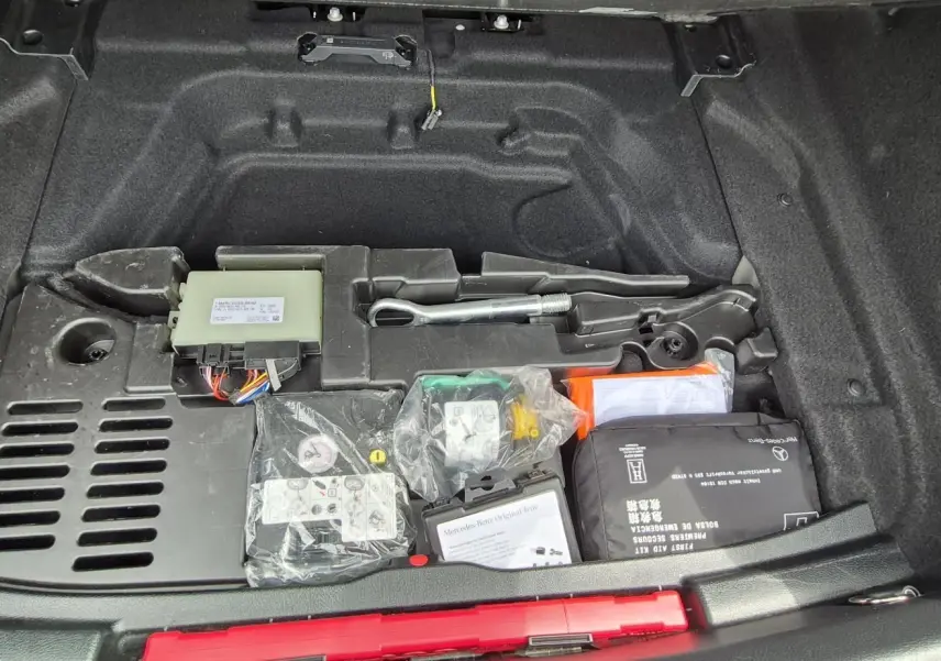 Coffre ouvert d’une Mercedes Classe A 180d gris foncé, montrant le kit anticrevaison et les outils de bord rangés sous le plancher.