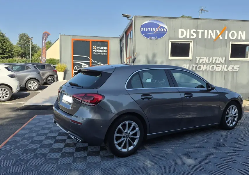 Mercedes Classe A 180d gris foncé vue 3/4 arrière droit, stationnée devant un bâtiment avec logo Distinxion.