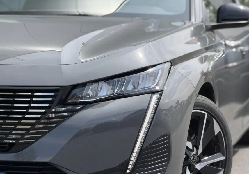 Gros plan sur l'avant droit gris Selenium du Peugeot 308 SW 2025, mettant en valeur le phare LED et la jante alliage 17 pouces.