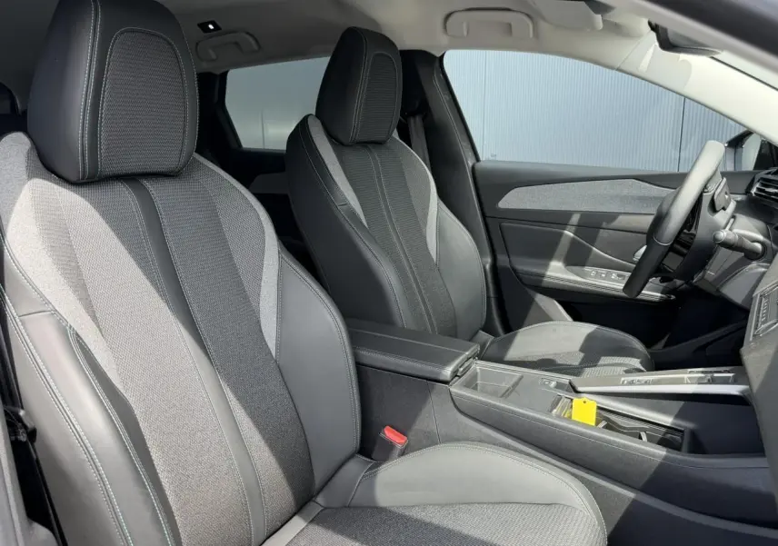 Vue intérieure côté droit du Peugeot 308 SW 2025, montrant les sièges bi-matière gris avec surpiqûres bleues et accoudoir central.