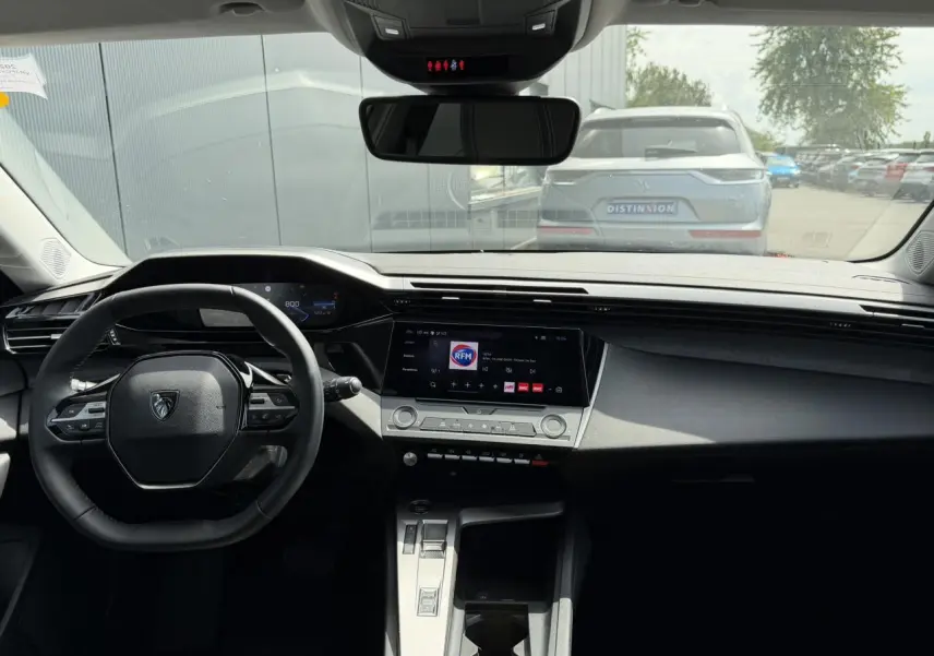 Vue intérieure frontale du poste de conduite de la Peugeot 308 SW 2025, avec tableau de bord noir et écran tactile central.