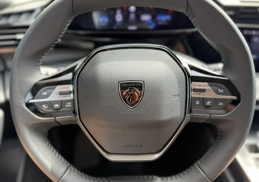 Gros plan sur le volant cuir noir du Peugeot 308 SW 2025 avec logo lion et commandes intégrées.