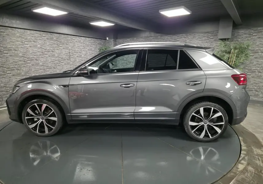Vue de profil côté gauche d'un Volkswagen T-Roc gris métallisé avec jantes alliage 19 pouces et finitions R-Line.
