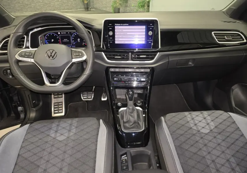 Vue intérieure frontale du tableau de bord et volant du Volkswagen T-Roc 1.5 TSI R-Line avec sellerie tissu et console noire brillante.