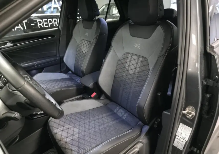 Vue intérieure côté gauche montrant les sièges avant gris avec surpiqûres et logo R-Line du Volkswagen T-Roc 2025.