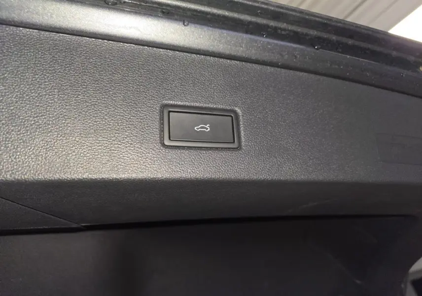 Gros plan sur le bouton d'ouverture électrique du hayon dans le coffre du Volkswagen T-Roc gris 2025 R-Line.
