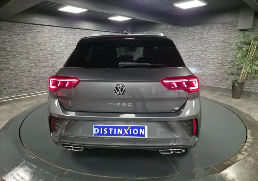 Vue arrière d'un Volkswagen T-Roc gris métallisé avec feux LED allumés et double sortie d'échappement chromée.