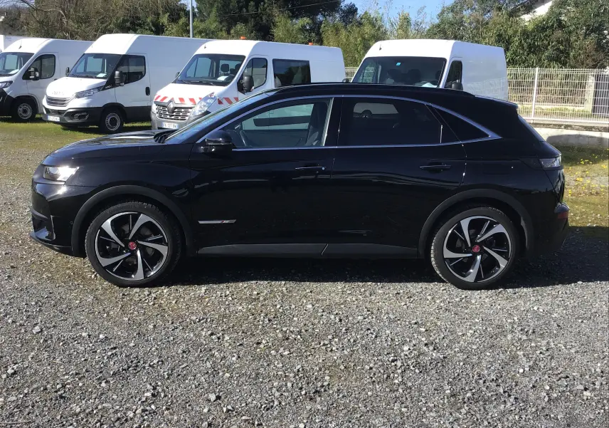 Vue de profil côté gauche d’un DS7 Crossback noir 2023 avec jantes alliage noires et chromées sur un sol gravillonné.