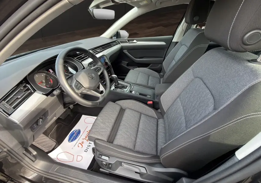 Vue intérieure côté conducteur de la Volkswagen Passat SW 2.0 TDI 2022 avec sièges tissu gris et volant multifonction cuir.