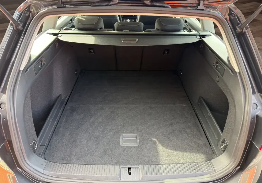 Coffre ouvert vu de l'arrière d'une Volkswagen Passat SW gris manganèse, espace de chargement vide et tapis noir.